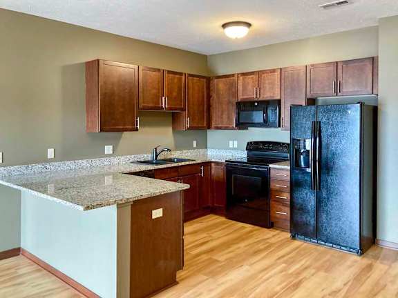 A kitchen with dark wooden cabinets, light granite countertops, black appliances, and peninsula.