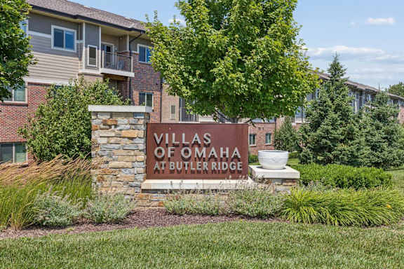Villas of Omaha at Butler Ridge apartment community entrance sign surrounded by landscaped greenery and residential buildings.