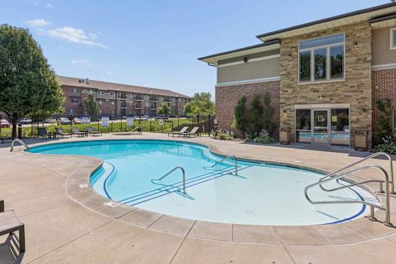 Outdoor swimming pool at Villas of Omaha at Butler Ridge with lounge chairs, entry steps, and the community clubhouse.