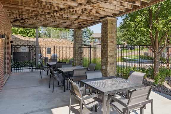 Covered outdoor seating amenity at Villas of Omaha at Butler Ridge with tables, chairs, stone columns, and landscaped views.