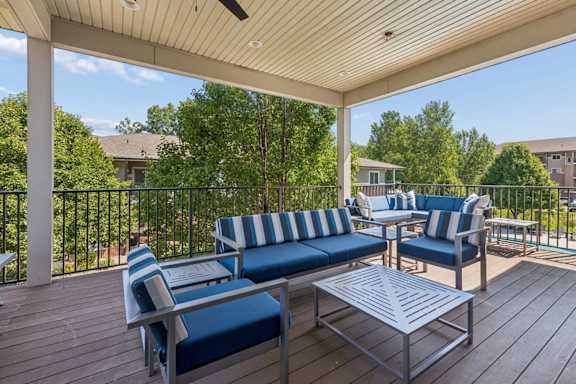 Covered outdoor lounge at Villas of Omaha at Butler Ridge with blue cushioned seating, tables, ceiling fan, and treetop views.