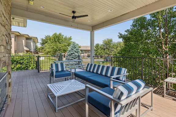 Covered outdoor lounge at Villas of Omaha at Butler Ridge with blue cushioned seating, tables, ceiling fan, and community views.