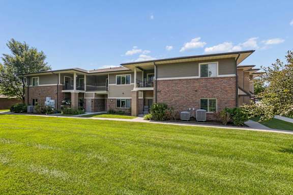 Apartment exterior with brick siding, private balconies, green lawn, and mature landscaping.