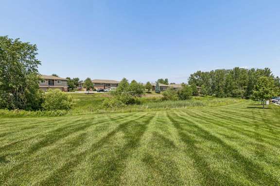 Expansive green lawn and natural landscaping at Villas of Omaha at Butler Ridge, with apartment buildings and mature trees beyond.