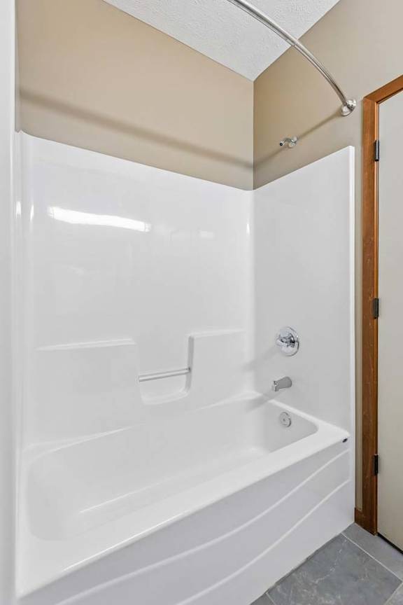Bathroom tub and shower combination with white surround, curved shower rod, built-in shelving, and chrome fixtures.