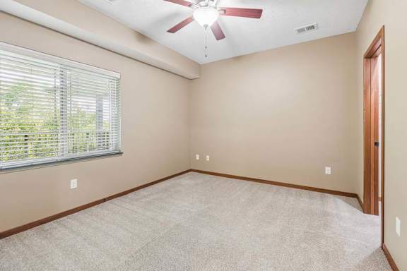 Carpeted bedroom with a large window, ceiling fan, neutral walls, and adjoining doorway.