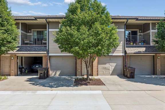 Apartment community exterior with private garages, covered balconies, mature trees, and individual driveways.