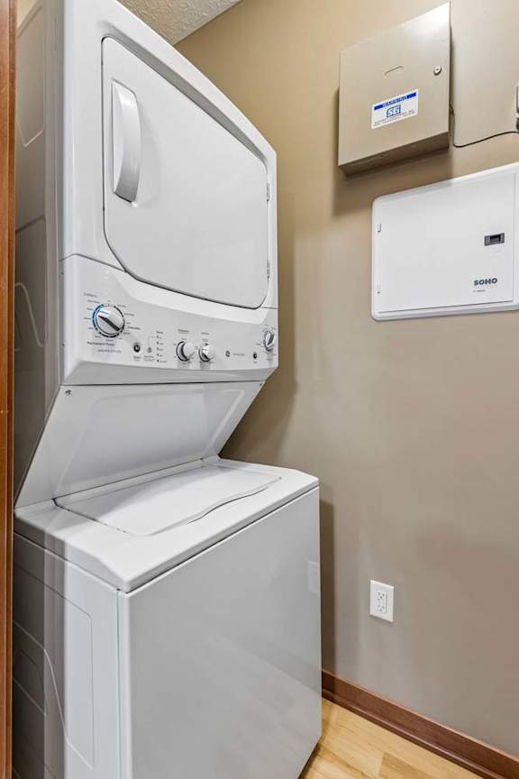 In-home laundry area with a stacked white washer and dryer, neutral walls, and wood-look flooring.