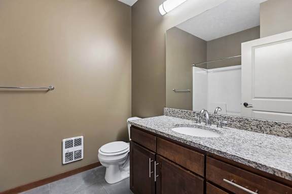 Apartment bathroom with a granite-look vanity, dark wood cabinetry, large mirror, neutral walls, and a tub-shower combination