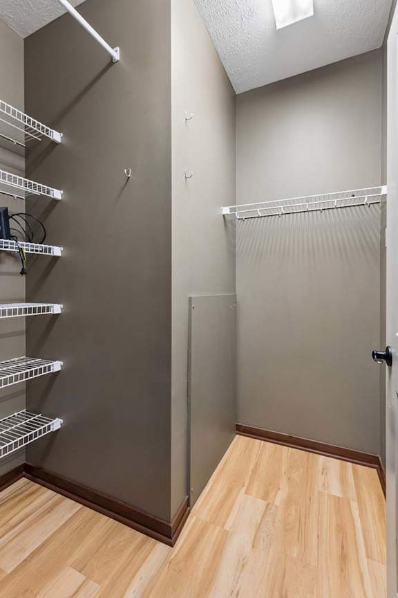 Walk-in apartment closet with wood-look flooring, neutral walls, wire shelving, hanging rods, and a high ceiling.