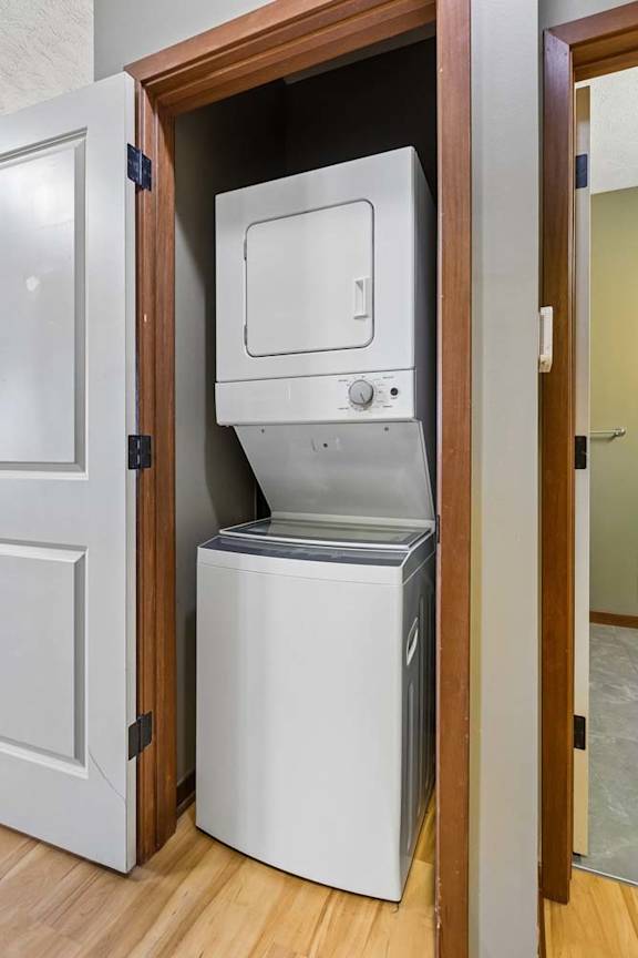 In-unit laundry closet with a stacked washer and dryer, wood-trimmed doorway, and wood-look flooring.