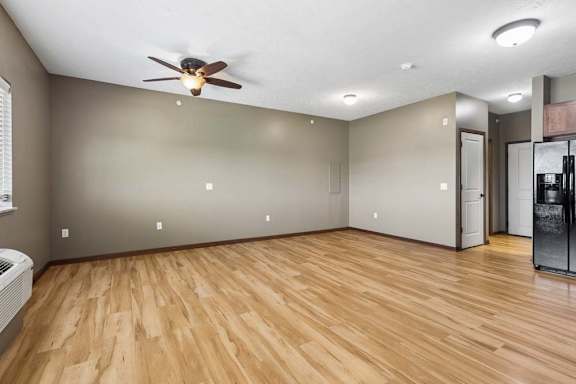 Bright, empty apartment living area with wood-look flooring, neutral walls, ceiling fan, and an open view into the kitchen.