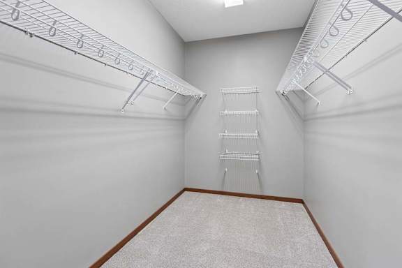 Spacious apartment walk-in closet with neutral carpet and extensive white wire shelving along three walls.