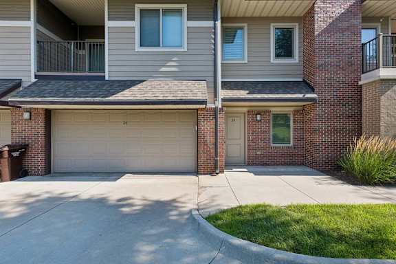 Unit exterior with brick and gray siding, an attached two-car garage, covered entry, and upper-level balcony.