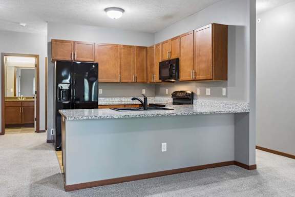 Kitchen with warm wood cabinetry, granite countertops, black appliances, and a spacious breakfast bar.