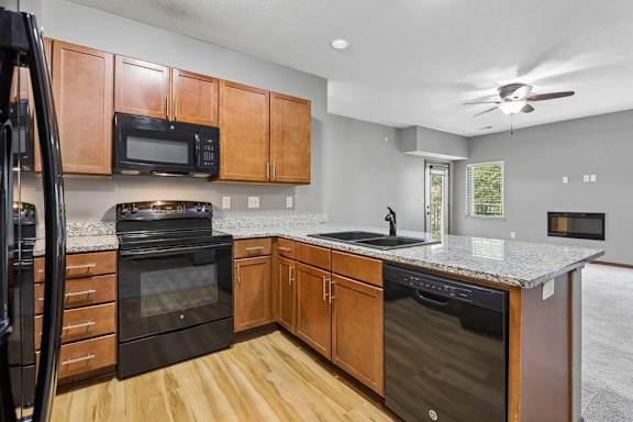 Open-concept kitchen with granite peninsula, black appliances, wood cabinetry, and views into the living area with fireplace.
