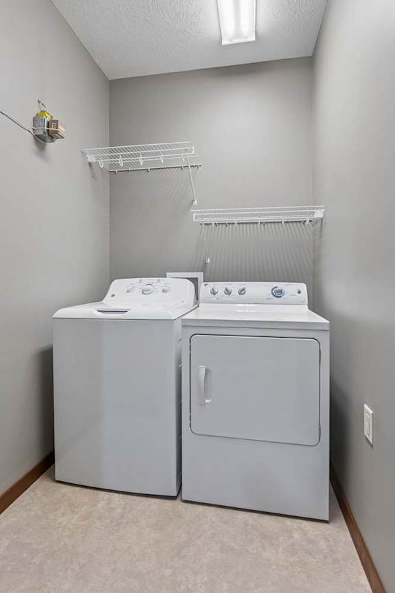 In-home apartment laundry room with a white washer and dryer, wall-mounted wire shelving, and neutral gray walls.