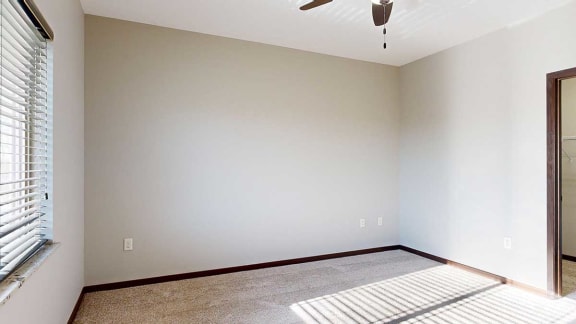 a carpeted bedroom with a ceiling fan, a large window, and an attached walk-in closet