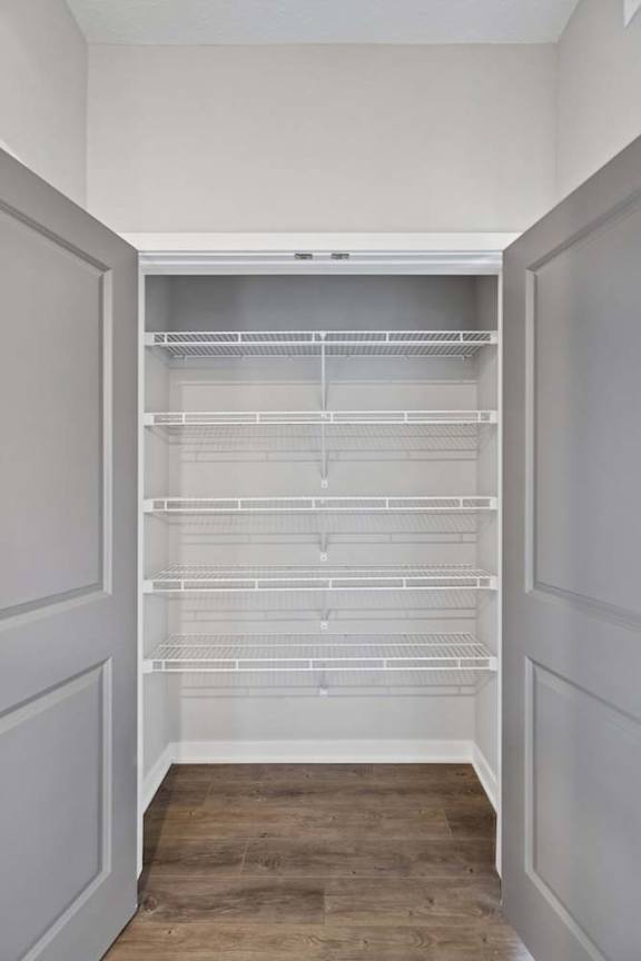 Apartment closet with double doors, built-in wire shelving, hanging rods, and wood-style flooring for convenient storage.