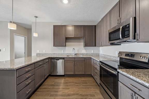 Modern apartment kitchen with dark cabinetry, granite-look countertops, stainless steel appliances, and a spacious U-shaped layout with ample counter space and storage.