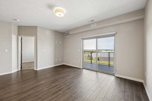 Bright apartment bedroom with wood-style flooring, a large sliding glass door leading to a private balcony, and abundant natural light.