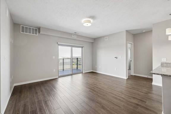 Spacious open-concept apartment living room with wood-style flooring, a large sliding glass door leading to a private balcony, and an adjoining kitchen with a breakfast bar.