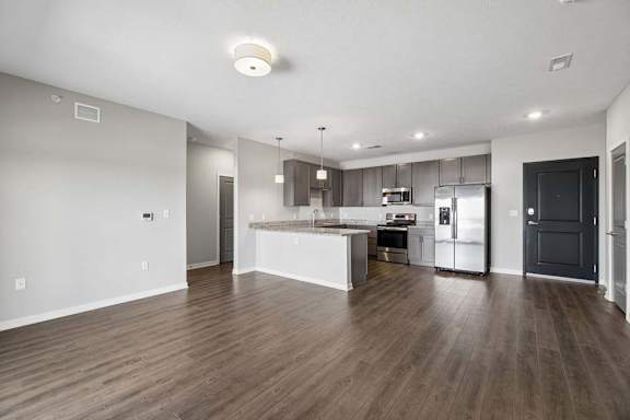 Spacious open-concept apartment living area with wood-style flooring, a modern kitchen featuring a large island, dark cabinetry, stainless steel appliances, and recessed lighting.