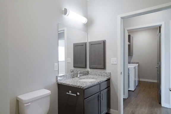 a bathroom with a sink and a mirror across a hallway from a laundry room