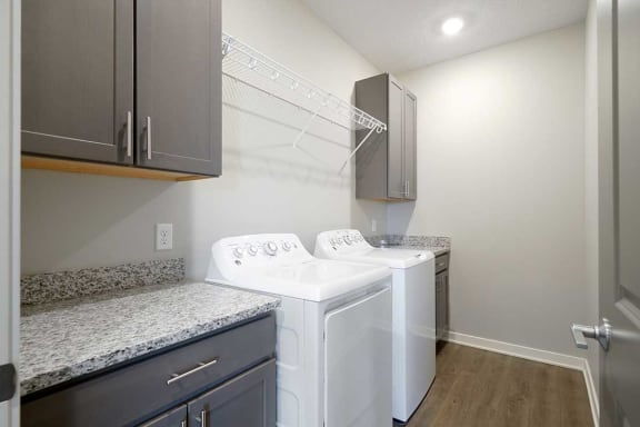 a large laundry room with a full-sized washer and dryer with over head shelving and cabinet storage