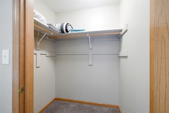 a walk in closet with a white wall and a shelf