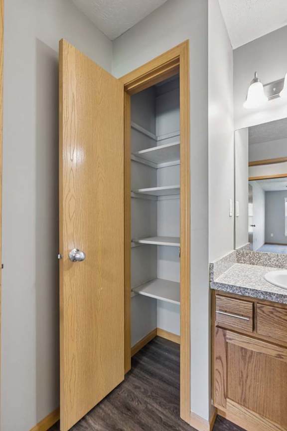 Built-in apartment pantry with open shelving, located beside the bathroom vanity with wood cabinetry and a stone-look countertop.
