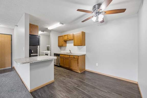 Open apartment dining area with wood-style flooring, a breakfast bar, ceiling fan, and adjoining kitchen with wood cabinetry.