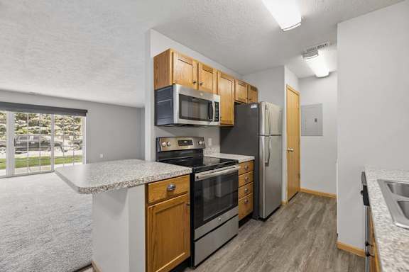 Apartment kitchen with wood cabinetry, stainless steel appliances, a breakfast bar, and an open layout overlooking the living room.