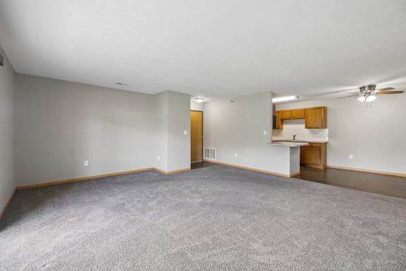 Expansive apartment living room with plush carpeting, an open breakfast bar, and a connected dining area and kitchen.