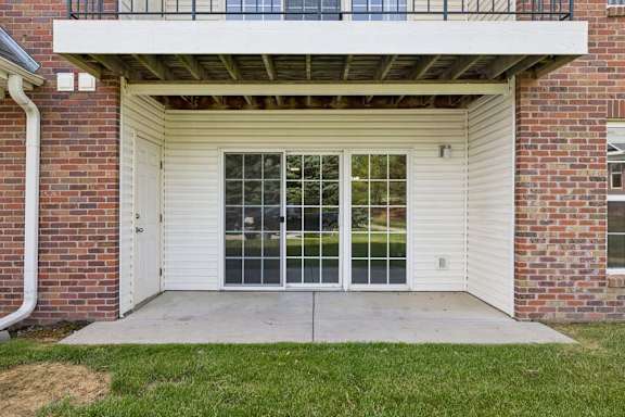 Covered ground-floor apartment patio with a concrete seating area, sliding glass door, and grassy lawn.