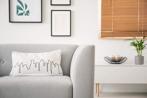 A grey couch with a white pillow that has a black city skyline design on it.