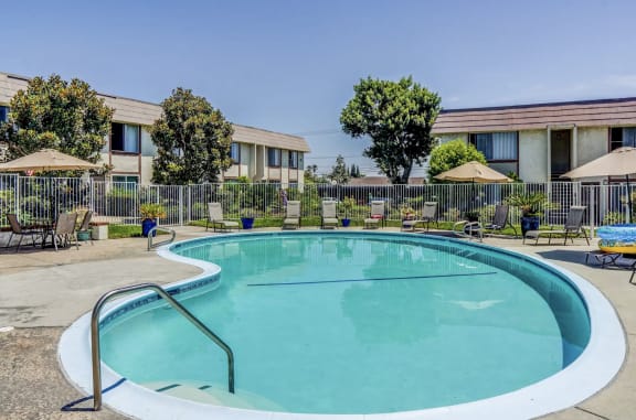 a swimming pool in front of a hotel with chairs and umbrellas