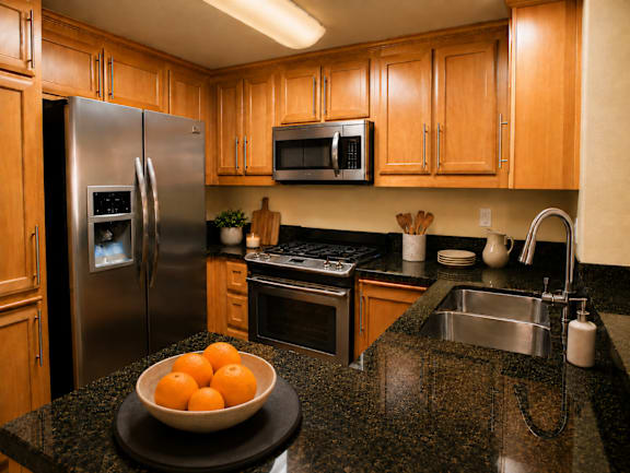A kitchen with a black granite countertop and a bowl of oranges on it.