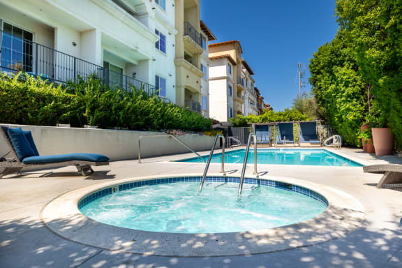 a hot tub and a pool with buildings in the background at Le Blanc Apartment Homes, Canoga Park
