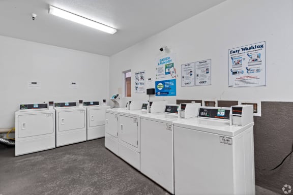 a row of washers and dryers in a laundromat with white machines at Dronfield Astoria Apartments, Sylmar, California, 91342