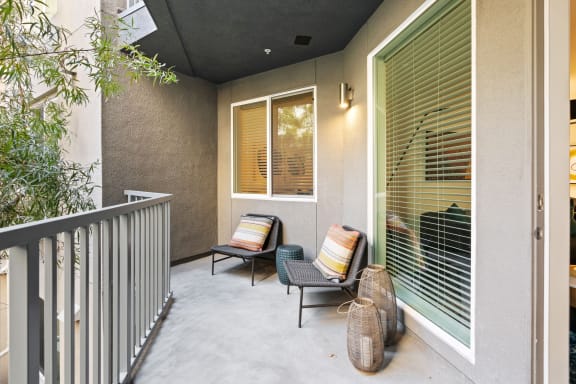 a balcony with two chairs and a window with blinds