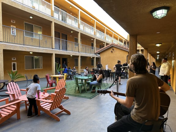 a man playing a guitar in a courtyard with people sitting at tables  at Dronfield Astoria Apartments ,Sylmar, California,  CA