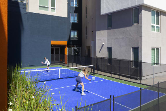 two women playing tennis on a blue court in front of a building