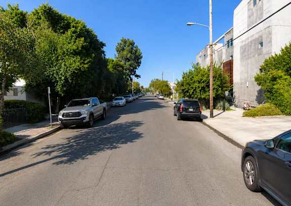 A street with cars parked on the side and trees lining the road.