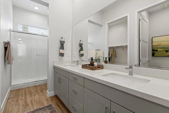 A bathroom with a white sink, a mirror, and a glass shower door at Village of Chandler Apartments, Chandler, AZ, 85249