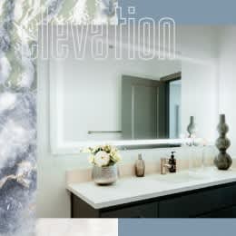 A bathroom with a marble wall and a large mirror above a double sink vanity.