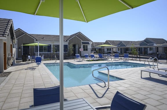 A pool surrounded by chairs and umbrellas in a sunny day. at Village of Chandler Apartments, Chandler, Arizona