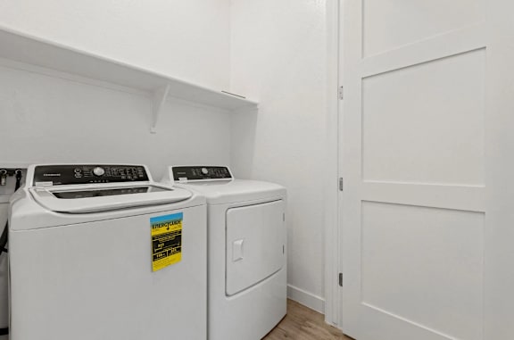Two white front loading washing machines in a laundry room. at Village of Chandler Apartments, Chandler, AZ, 85249