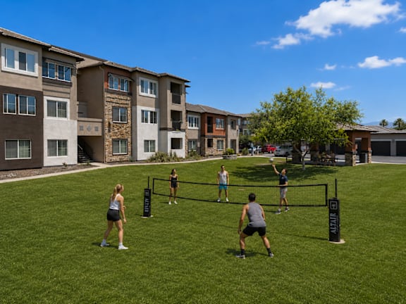 A group of people playing volleyball in a grassy area in front of apartment buildings.