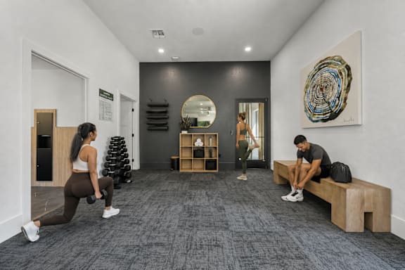 A woman is doing squats in a gym with a man sitting on a bench.